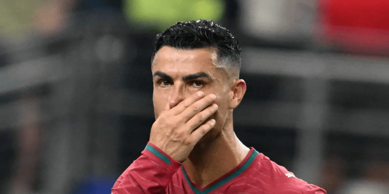 Soccer player in a red jersey covering his mouth with his hand during a match.