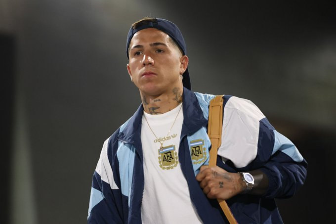 Young man in a white shirt and blue windbreaker with a tan shoulder bag, wearing a backward cap.