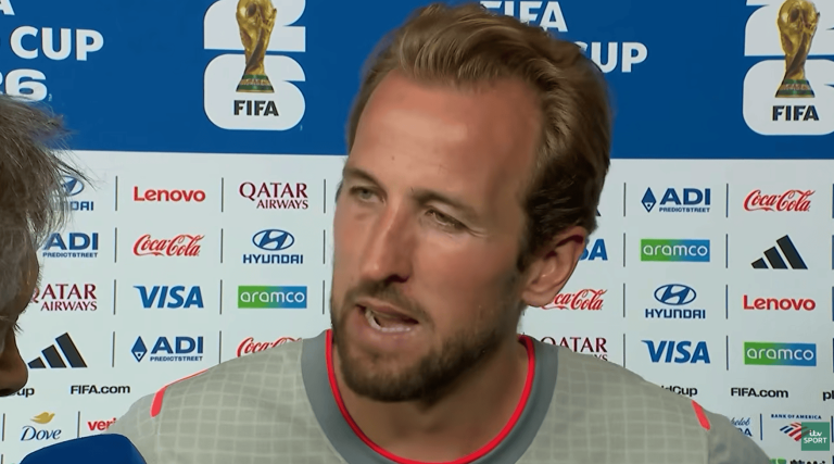 Male footballer speaks during a post-match interview, backdrop shows FIFA branding and sponsor logos behind him.