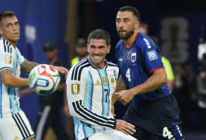 Argentina midfielder in light-blue stripes battles a French defender in blue during a soccer match, ball nearby and players contending for possession.