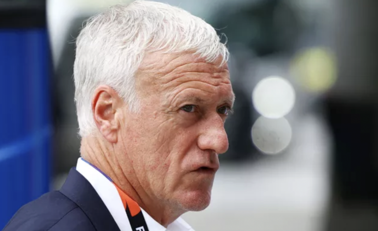 Older man with short white hair wearing a dark suit, white shirt, and an orange lanyard, looking to the left outdoors.