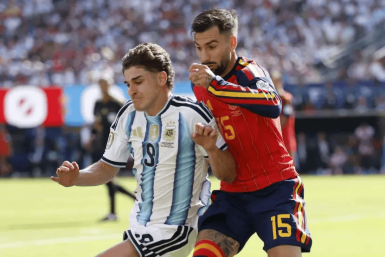 Two soccer players race for the ball during a match, one in Argentina’s light blue and white jersey and the other in a red kit with number 15, in a crowded stadium.