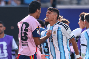 Two soccer players argue angrily on the field, one in a blue-and-white Argentina jersey and the other in a pink training bib.