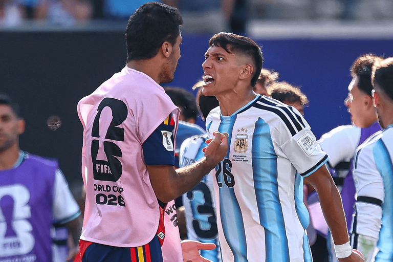 Two soccer players argue angrily on the field, one in a blue-and-white Argentina jersey and the other in a pink training bib.