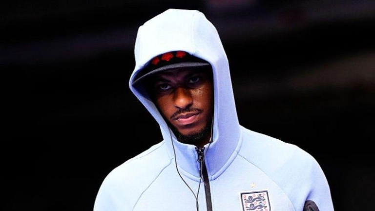 Man wearing a light blue hoodie with England crest, hood up, looking at the camera.
