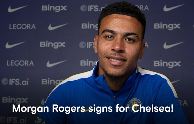 Morgan Rogers signs for Chelsea, posing in a blue Chelsea training top in front of a sponsor backdrop.