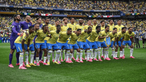 Brazil men's national soccer team lines up for a team photo on the field before a World Cup match, wearing yellow jerseys and blue shorts with pink cleats.