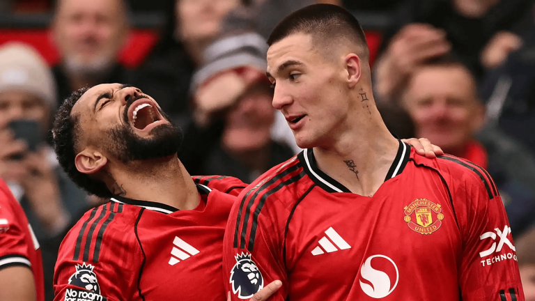 Two Manchester United players in red jerseys celebrate together, one with mouth wide open in a cheer while the other smiles at him.