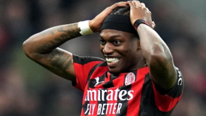 Soccer player in AC Milan kit holding his head with a smile during a match, celebrating relief or joy.