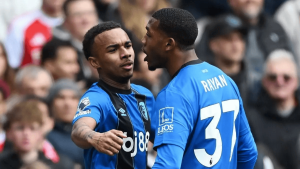 Two football teammates in blue jerseys celebrate on the field as a crowd watches in the background.