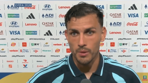 Close-up of a male football player giving an interview in front of sponsor logos at a press event.