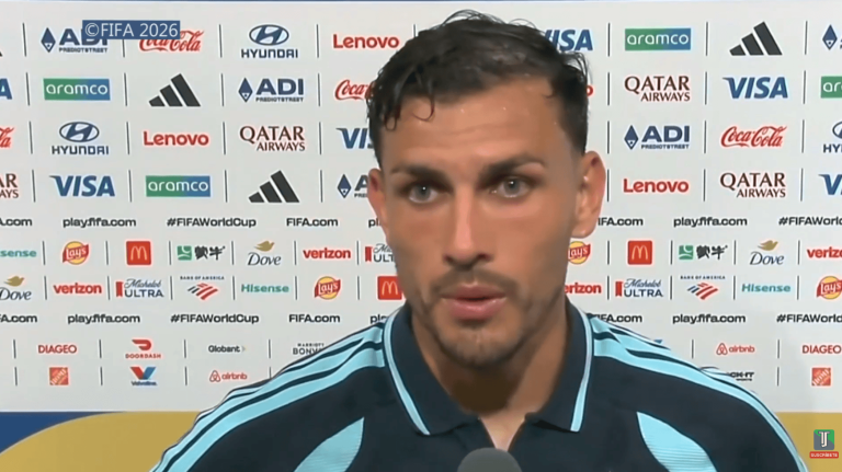 Close-up of a male football player giving an interview in front of sponsor logos at a press event.