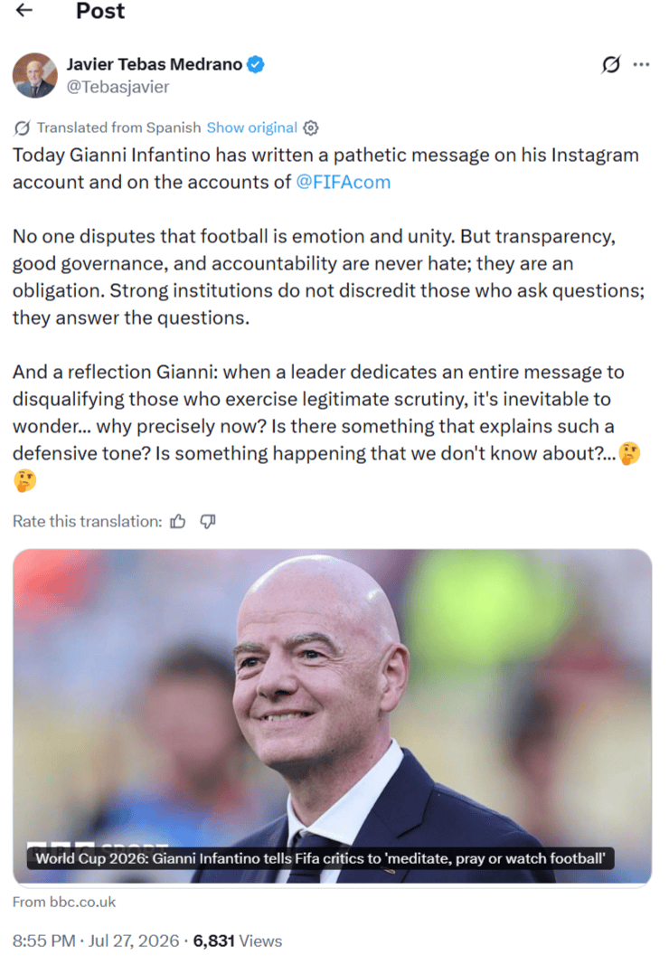 Close-up of FIFA President Gianni Infantino smiling in a suit at an event, with a bottom caption about World Cup 2026 telling critics to meditate, pray, or watch football
