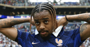 French national team footballer with braided hair, hands behind his head, standing on the pitch in a blue jersey.