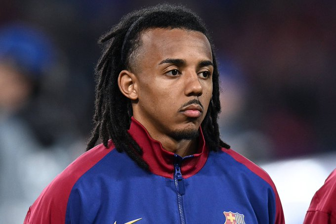 Male footballer wearing a blue and maroon FC Barcelona training jacket, looking thoughtful on the field.
