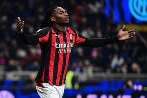 Soccer player in a red-and-black AC Milan jersey with arms outstretched celebrating on the pitch.
