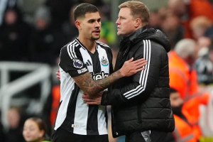 Soccer player in Newcastle United kit embraces a man in a black puffer jacket on the sideline.