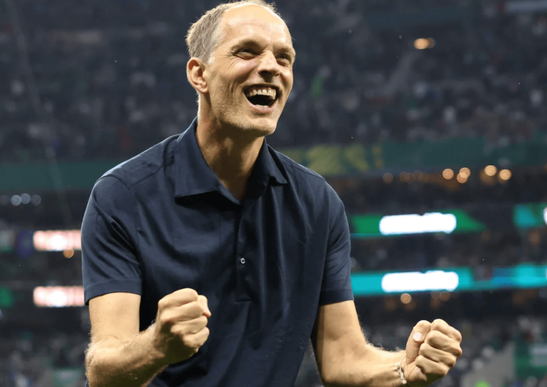 Man in a navy polo celebrates with fists clenched at a stadium, smiling in triumph.