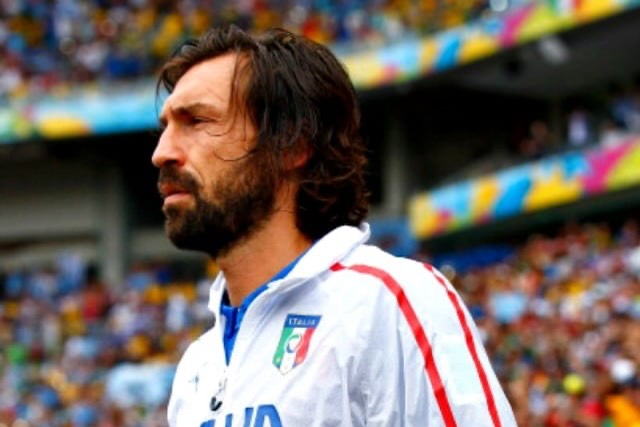 Bearded man in a white Italy soccer jersey with blue trim on a crowded stadium field, profile view.