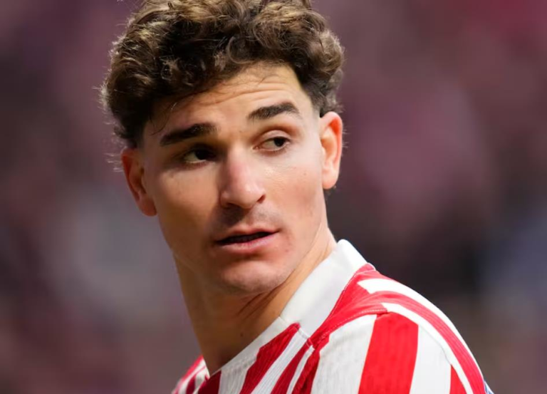 Portrait of a male soccer player with short dark hair in a red-and-white striped jersey, looking to the left.
