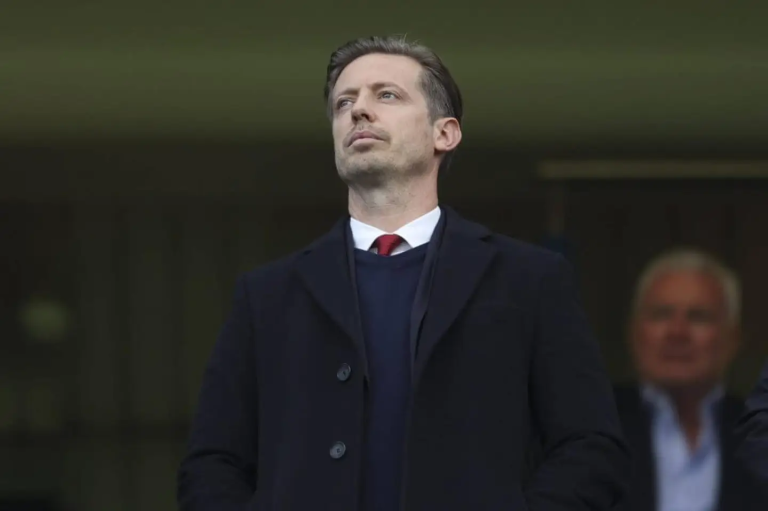 Man in a dark overcoat with a red tie gazing upward at an outdoor event.
