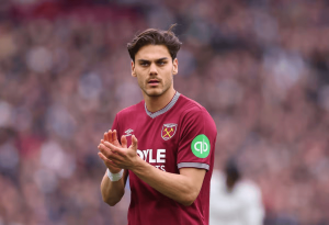 West Ham United player in a claret away kit clapping on the pitch with a blurred crowd in the background, during a match.