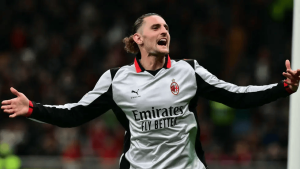 Soccer player in a Milan jersey celebrating with arms outstretched on the pitch.