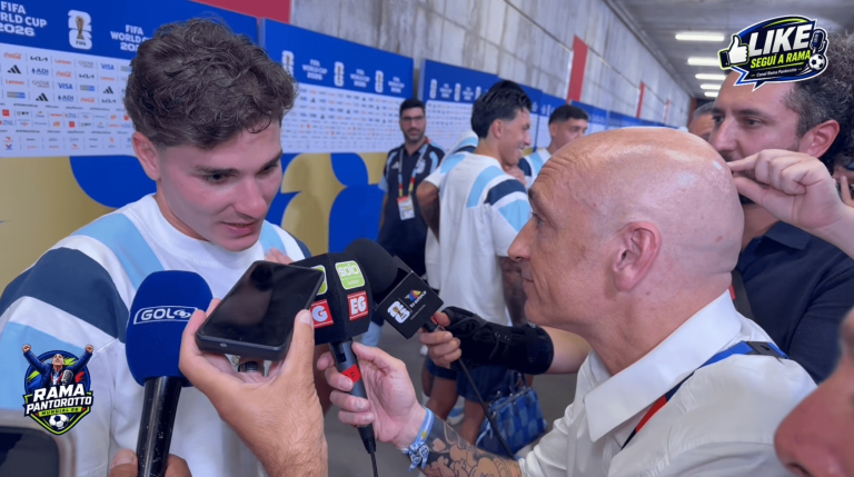 Reporter interviewing a footballer in a light-blue striped jersey, several branded microphones thrust toward him in a press area. (informative)