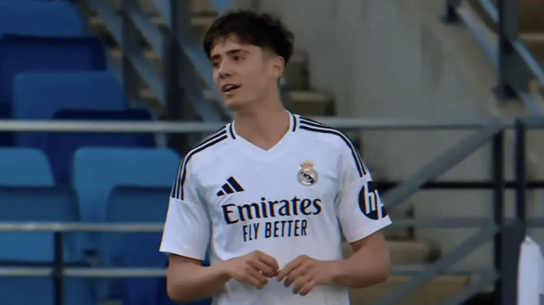Young man in a white Real Madrid jersey standing in a stadium with blue seats in the background