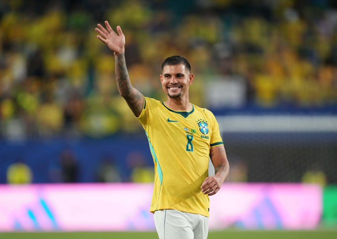 Brazilian footballer in a yellow Brazil shirt with number 8 waves to fans on the field.