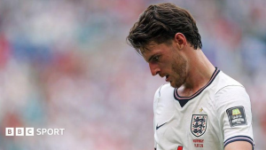 Close-up of a male soccer player wearing a white England jersey, head bowed, on a blurred field; BBC Sport logo in the corner.