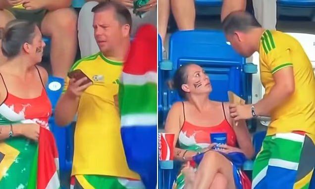 Two spectators in green‑yellow outfits converse with a seated woman in a red dress and face paint at a stadium stands.