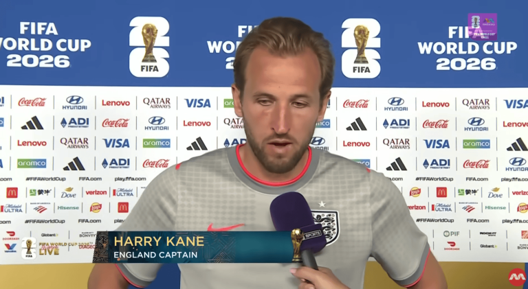 Harry Kane, England captain, speaks at a FIFA World Cup press conference with sponsor logos behind him.