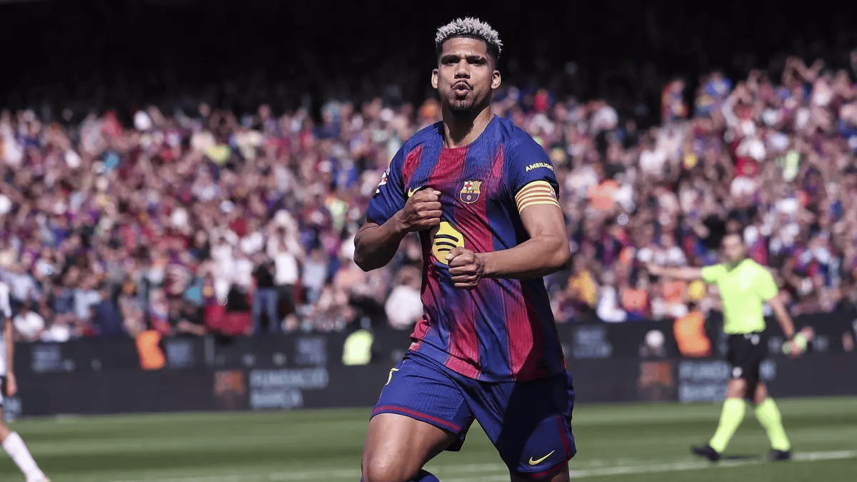 Soccer player in Barcelona jersey celebrating a goal on the pitch with a cheering crowd behind him.