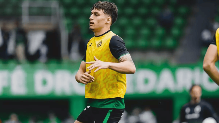 Soccer player wearing a yellow training bib jogs on a green stadium field during practice.